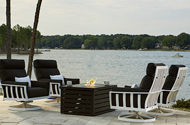 Lakefront patio with four cushioned chairs around a table with a firepit in the center