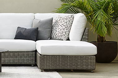 woven brown couch topped with white cushions beside a potted palm
