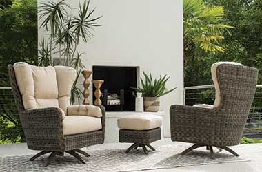 high backed woven brown chairs topped with tan cushions by an outdoor fireplace