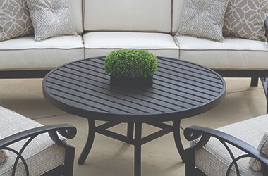 round, dark colored table surrounded by cushioned patio couch and two chairs