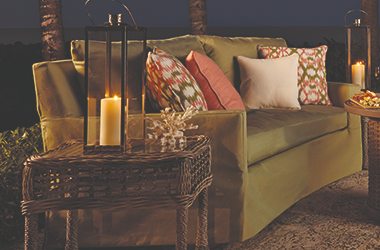 candlelit green sofa on a patio with wicker side table