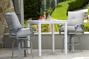 Tall white table set with food a drink and two gray chairs on a patio