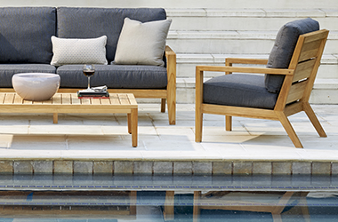 poolside light wooden cocktail table, sofa and chair with dark gray cushions