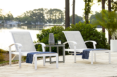 two white reclined chaises and a side table near the lake