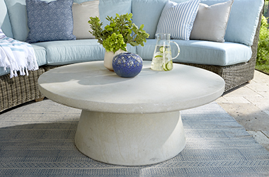 round stone white table in front of woven couch with light blue cushions