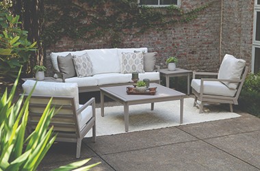 light brown cocktail table, two chairs and sofa with white cushions against a brick wall on a patio